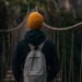 Une personne vue de dos traverse un pont de corde au-dessus d’un ravin, symbole du courage et de la confiance retrouvée.